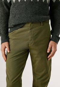 Zelené bavlnené nohavice s textúrovaným povrchom, so zapínaním na gombík a bočnými vreckami. Nosia sa s tmavým svetrom so vzorom.