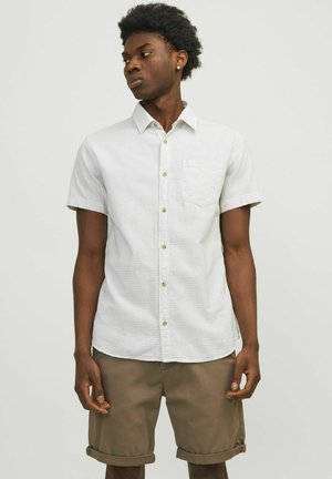 Camisa de botón de manga corta de color claro con un acabado texturizado y un bolsillo en el pecho, combinada con pantalones cortos beige remangados.