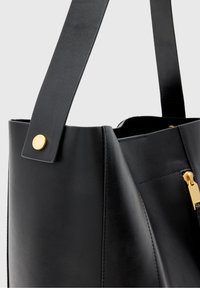 Czarna skórzana torebka o strukturalnym designie, gładkiej fakturze, złotych metalowych akcentach oraz wyraźnym pasku na ramię z przeszyciem.
