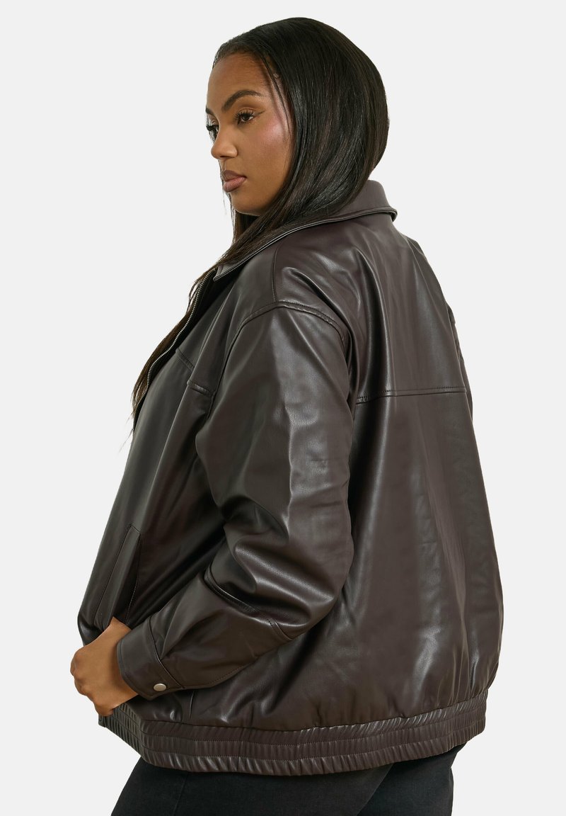 Giubbotto bomber in pelle marrone con vestibilità rilassata, vita a coste, tasche laterali e colletto. Texture liscia e design minimalista.