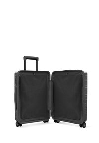 Valise rigide noire avec une poignée rétractable, deux compartiments zippés doublés de maille, et quatre roues pivotantes pour la mobilité.