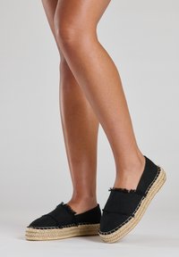 Zwarte canvas espadrilles met rafelige randen, een jute touwzool en contrasterende witte stiksels. Glad textuur, instapontwerp.