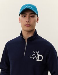 Felpa blu navy con zipper e logo bianco "LD" sul petto abbinata a un berretto blu brillante con scritta ricamata bianca.