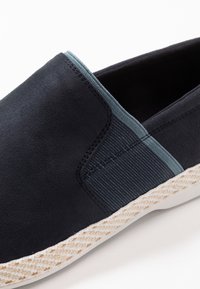 Scarpa navy slip-on con pannello elastico laterale, tomaia testurizzata e suola intermedia simile al juta intrecciata. Finitura liscia con accenti in azzurro chiaro a contrasto.