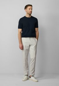 Marineblaues Kurzarmhemd, hellgraue maßgeschneiderte Hose und weiße Sneaker mit schwarzen Akzenten. Schlichtes, modernes Design und taillierte Silhouette.