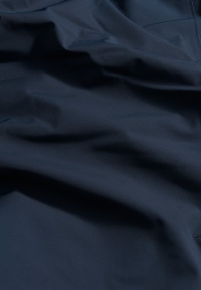 Sjöblått tyg med en jämn, lätt reflekterande yta, som har subtila veck och skrynklor, vilket skapar en känsla av djup och dimension.