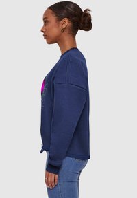 Felpa blu navy con vestibilità rilassata, scollo rotondo e polsini a costine. Presenta una stampa grafica e dettagli con cordino sull'orlo.