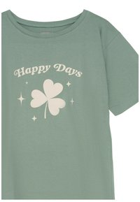 Zielony bawełniany t-shirt o luźnym kroju, z białym napisem "Szczęśliwe Dni" i jasnym graficznym motywem koniczyny na środku.