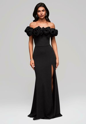 Svart off-the-shoulder klänning med volangig byst, figurnära silhuett och midinggi spår. Tillverkad av slät tyg, golvlång design.