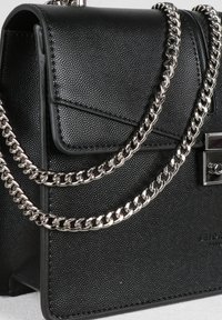 Borsa a tracolla in pelle nera strutturata con pattina pieghevole, tracolla in catena argentata e accessori in metallo. Presenta una forma rettangolare elegante.