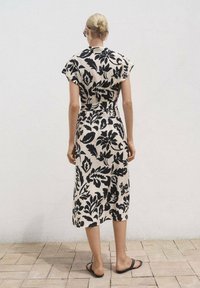 Robe midi à motifs floraux noirs et crème avec des manches courtes, taille cintrée et silhouette droite, assortie de sandales plates.