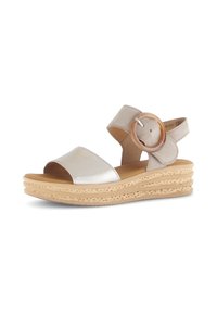 Sandale beige avec une sangle métallique et une grande boucle circulaire. Présente une semelle compensée épaisse et texturée avec un design en couches.