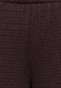 Tissu texturé brun foncé avec un motif froissé et ondulé, probablement une partie de vêtement ou de tapisserie.