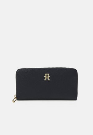 Portafoglio in pelle nera con texture a granularità, accentuato da un logo dorato e chiusura a zip. Forma rettangolare con dettagli di cucitura lungo i bordi.