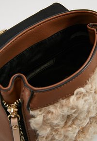 Brown faux leather bag with textured beige fabric front, black top, gold zipper, and interior lining. Compact design with a zip closure.