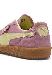 Baskets Puma en daim rose avec bande latérale beige et logo au talon, semelle en gomme couleur chewing-gum et étiquette de taille visible à l'intérieur du col de la chaussure.