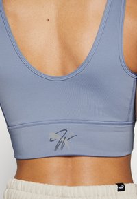 Gros plan du dos d’une personne portant un soutien-gorge de sport violet clair avec un logo Puma et un pantalon clair avec une étiquette Puma.