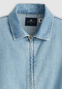 Ljusblå denimjacka med dragkedja, spetsig krage och vertikala sömdetaljer. Har varumärkesetikett inuti nacken.