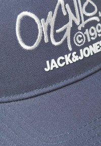 Gorra azul marino hecha de tela texturizada, con logotipos y acentos bordados en blanco, con visera curva y costuras detalladas.