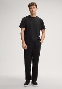 Schwarzes, passendes T-Shirt und Hose aus strukturiertem Stoff mit einem dezenten Muster. Das T-Shirt hat einen Rundhalsausschnitt; die Hose ist gerade geschnitten.