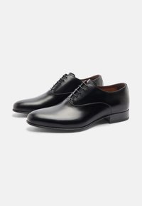 Scarpe in pelle nera con una texture liscia, punta affusolata e allacciatura con cinque occhielli. Presentano un tacco basso e un design minimalista.