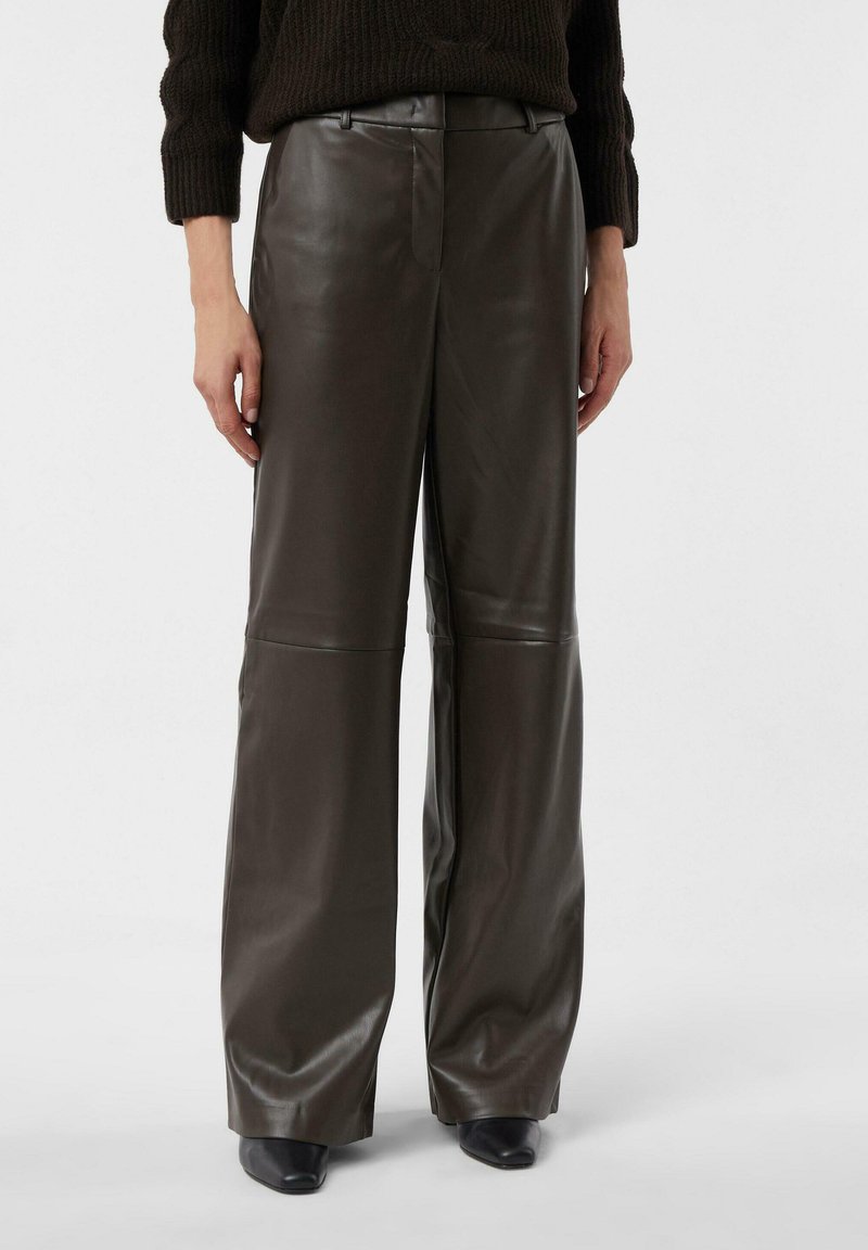 Wide-leg trousers in dark brown leather. Smooth texture with a high waist and creased detailing. Paired with black heeled shoes.