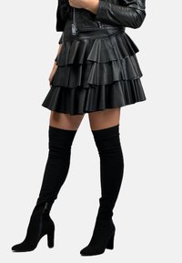 Czarna, skórzana mini spódnica z warstwowymi falbanami. Połączona z czarnymi skarpetkami za kolano oraz botkami na obcasie, prezentując elegancki design.