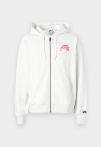Sweatshirt branca com fecho éclair, feito de um tecido suave, com um logo bordado em rosa "Nike SB" no peito e um logo preto no punho esquerdo.
