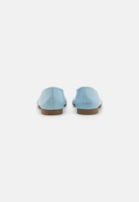 Světle modré kožené nazouvací boty s nízkou hnědou podrážkou, zaoblenou špičkou a hladkým povrchem. Minimalistický design, žádné viditelné kovové prvky nebo akcenty.