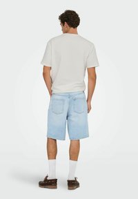 Lysblå denimshorts med lige snit, to baglommer, parret med en grå kortærmet skjorte og brune bådsko.