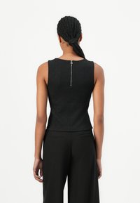 Zwarte mouwloze top met een gestructureerd patroon, getailleerd silhouet en een ritssluiting aan de achterkant. Gecombineerd met zwarte wijde broek.