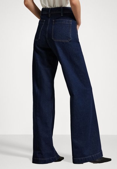 Pantaloni di jeans blu scuro, a gamba larga, con vita a media altezza, due tasche posteriori e cuciture a contrasto. Il tessuto ha una leggera trama.