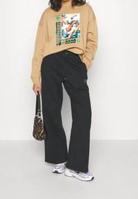 Felpa beige oversize con stampa grafica, pantaloni neri a gamba larga e scarpe da ginnastica con dettagli viola. Borsa piccola con stampa animalier.