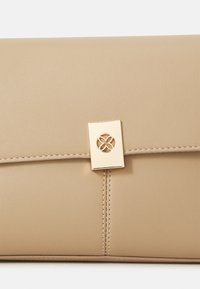 Beige clutchveske laget av glatt lær, med gullhåndtak og et blomstermønster i utskjæring, samt synlige sømmer langs kantene.