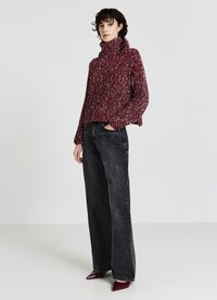 Burgunderfarbener Strickpullover mit hohem Kragen und weit geschnittenen Ärmeln, kombiniert mit hoch taillierten schwarzen Schlagjeans und glänzenden burgunderfarbenen Absätzen.