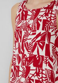 Czerwono-biała bluzka na ramiączkach z geometrycznym wzorem liści, wykonana z lekkiego materiału, z okrągłym dekoltem i bez rękawów.