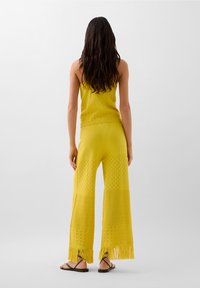 Ensemble en tricot jaune composé d'un haut court à bretelles spaghetti et d'un pantalon large avec franges et motifs texturés.