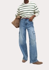 Gestreifter grün-weißer Pullover, hellblaue Cargo-Jeans mit Seitentaschen und beige Schuhe. Der Pullover hat einen hohen Kragen.