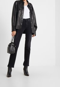 Camisa chaqueta de cuero negro con botones a presión, camiseta ajustada blanca debajo, jeans rectos negros, botas de tacón negro y bolsa tipo cubo con tachuelas.