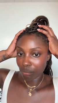 Gros plan d'une personne avec des cheveux tressés portant plusieurs colliers en or. La peau semble lisse ; les épaules sont visibles, arborant un haut blanc.