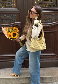 Geltona petneša su metaliniais kaiščiais, béžinė ilgomis rankovėmis marškiniai, šviesiai mėlyni džinsai, saulėgrąžos rudos popieriaus pakuotėje ir geltoni sandalai.