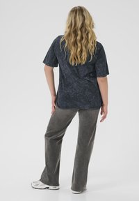 Oversized dark gray t-shirt with a textured finish, paired with loose-fitting gray pants and white sneakers. Visible back design.