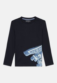 Navy blue long-sleeve t-shirt with a partially visible white and blue GUESS logo graphic on the lower front side.