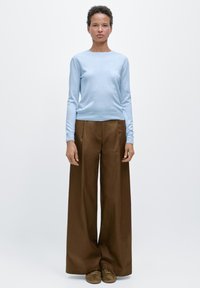 Lichtblauw trui met lange mouwen en een ronde hals, gecombineerd met hooggetailleerde, brede bruine broek en bruine suède schoenen.
