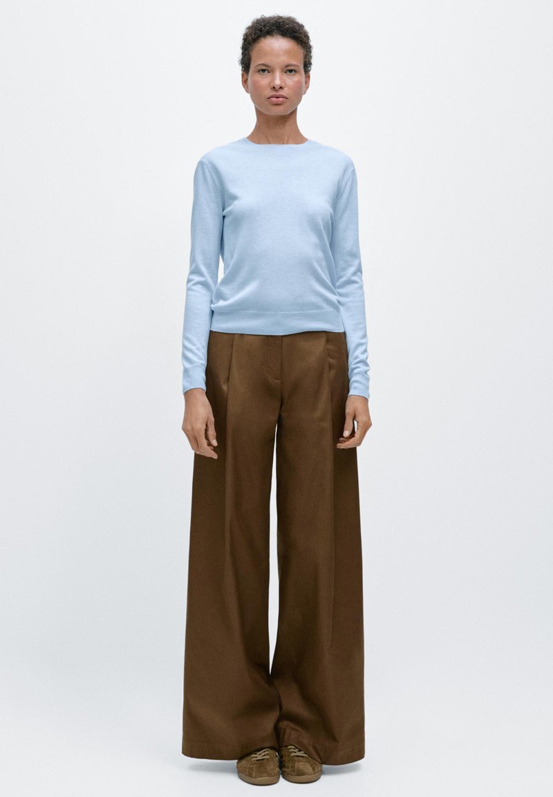Lichtblauw trui met lange mouwen en een ronde hals, gecombineerd met hooggetailleerde, brede bruine broek en bruine suède schoenen.