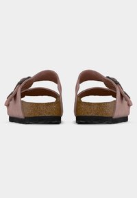 Ζεύγος ροζ σανδαλιών από καστόρι με πέλματα φελλού, μαύρες σόλες και ρυθμιζόμενους ιμάντες με αγκράφα, εμφανίζονται από πίσω σε λευκό φόντο.