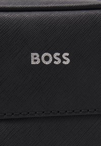 Juodas tekstūruotas audinys su iškilniu sidabro spalvos "BOSS" logotipu. Papuoštas švariomis linijomis ir subtiliu siuvinėjimo detalizavimu.