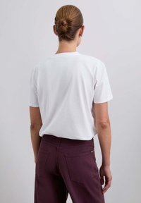 Camiseta blanca de algodón con un corte holgado, mangas cortas y cuello redondo, combinada con pantalones color ciruela que tienen bolsillos traseros.