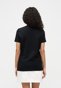 Μαύρο μπλουζάκι με κοντό μανίκι, εμφανιζόμενο από πίσω, με στρογγυλή λαιμόκοψη και υφή από απαλό βαμβάκι, συνδυασμένο με λευκή φούστα.