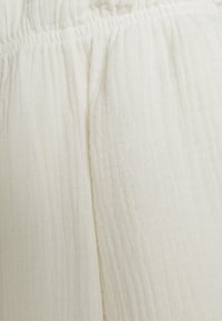 Tecido branco com uma superfície texturizada e enrugada. O material é leve e macio, apresentando uma cintura franzida para um uso flexível.